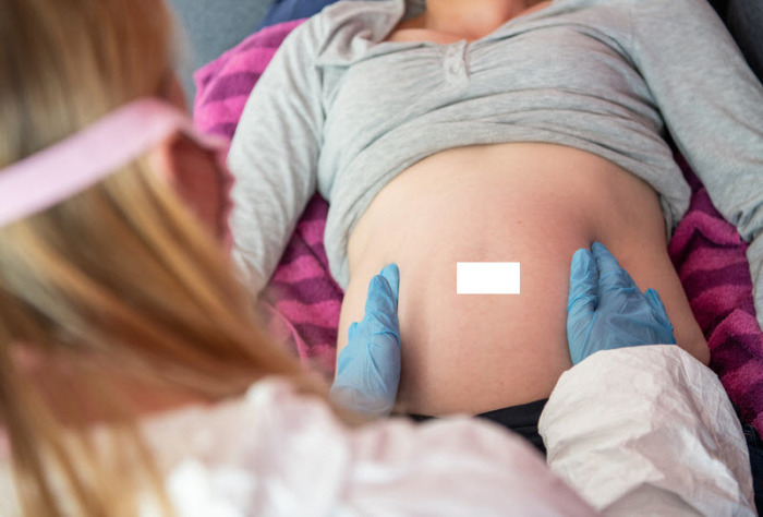 Eine Hebamme trägt Schutzausrüstung und untersucht eine schwangere Frau. (zu dpa «Schwangere mit Corona: seltener Fieber, aber mehr frühe Geburten») Foto: Caroline Seidel/dpa
