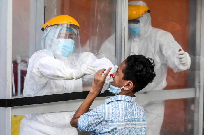 Indonesische Sanitäter in Schutzanzügen nehmen Speichelproben von einem Jungen während eines Koronaviren-Austausch-Tests in Medan. Foto: epa/Dedi Sinuhaji