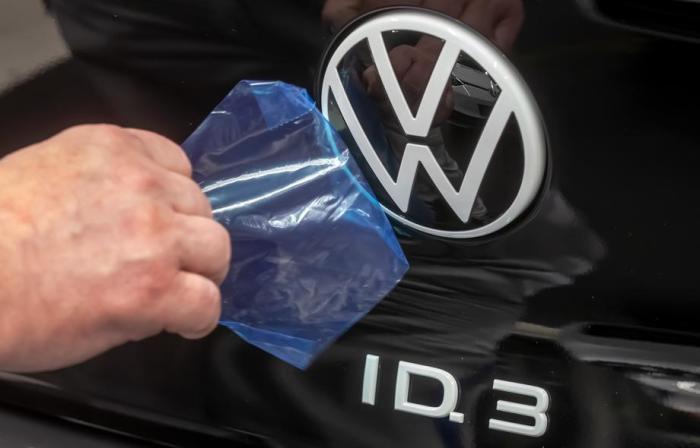 Ein Mitarbeiter von Volkswagen zieht eine Schutzfolie vom VW-Logo an einem Volkswagen ID.3 in der Montagelinie ab. Foto: epa/Uwe Meinhold