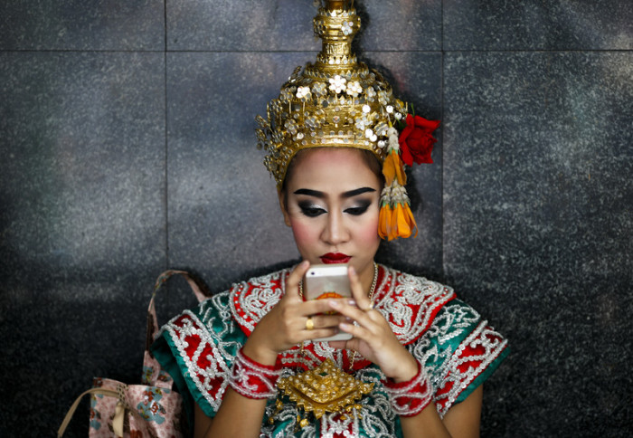 Eine Erawan-Tänzerin kommuniziert mit ihrem Smartphone. Foto: epa/ Rungroj Yongrit