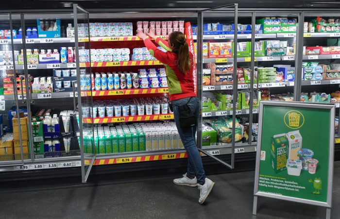 Ein Mitarbeitern ordnet die Milchprodukte in einem Kühlregal im Lebensmittel-Discounter Penny, vor dem der Aufsteller mit der Werbung der Kampagne «Kostbares retten» steht. Foto: Jens Kalaene/Dpa