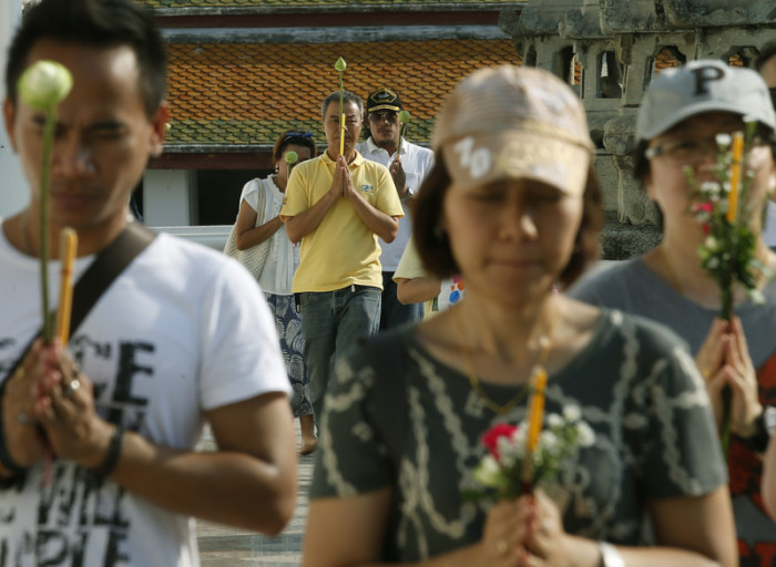 Mit einem Gebet werden Blumen, Räucherstäbchen und eine brennende Kerze dreimal um den Tempel getragen. Foto: epa/Narong Sangnak