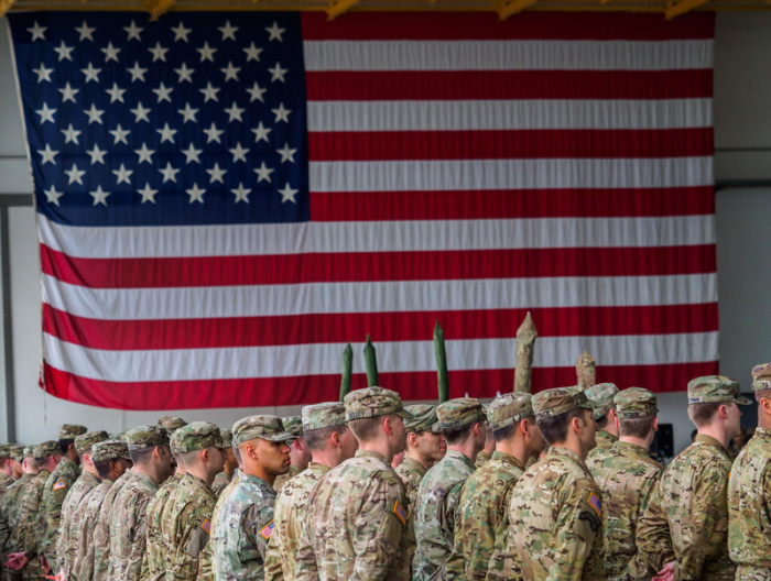US-Soldaten stehen während einer militärischen Zeremonie in den Storck-Barracks vor einer Flagge der Vereinigten Staaten von Amerika. US-Präsident Donald Trump will Deutschland mit einem Teilabzug der US-Truppen für die... Foto: Nicolas Armer/dpa