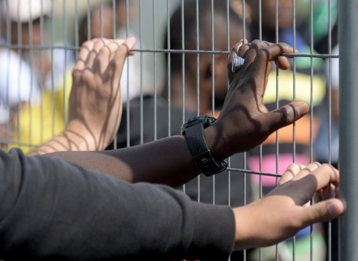 Manching, Bayern: Im Transitzentrum für Asylsuchende halten Hände von Sicherheitskräften einen Zaun fest. Foto: Stefan Puchner/Dpa
