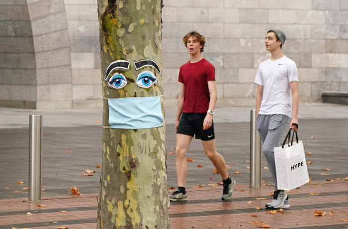 In Melbourne gehen Menschen an einem Baum mit einer Gesichtsmaske und angehefteten Augen vorbei. Foto: epa/Scott Barbour