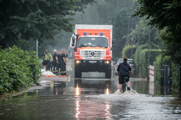 Nordrhein-Westfalen, Düsseldorf: Ein Fahrradfahrer fährt durch eine überflutete Straße in der Ostparksiedlung. Foto: Henning Schoon/dpa