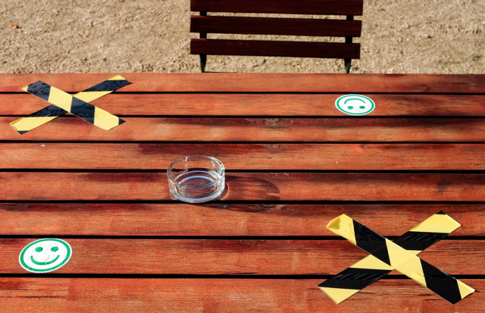 Auf einem Tisch eines Freiluftcafes steht zwischen aufgeklebten Kreuzen und Smileys für den Corona-Abstand ein leerer Aschenbecher. Foto: Jens Kalaene/dpa-zentralbild/dpa
