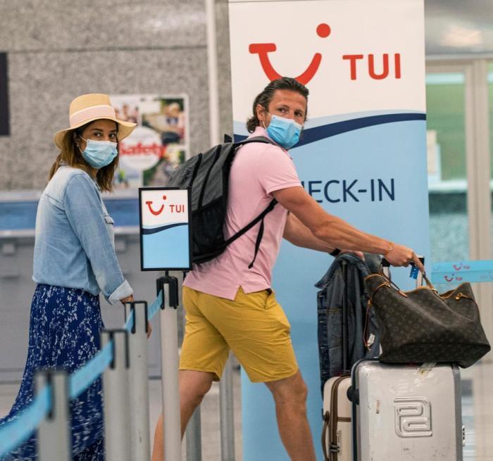 Reisende mit ihrem Gepäck gehen neben einem Stand des Reiseunternehmens TUI auf dem Flughafen von Palma de Mallorca in Palma. Foto: epa/Cati Cladera