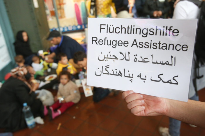 Ein freiwilliger Helfer hält im Hauptbahnhof in Hamburg ein Schild auf deutsch, englisch und arabisch, auf der Hilfe für Flüchtlinge angeboten wird. Foto: Bodo Marks/Dpa
