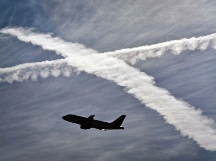Ein Flugzeug startet vom Flughafen vor zwei Kondensstreifen am Himmel, die sich kreuzen. Foto: Frank Rumpenhorst/Dpa