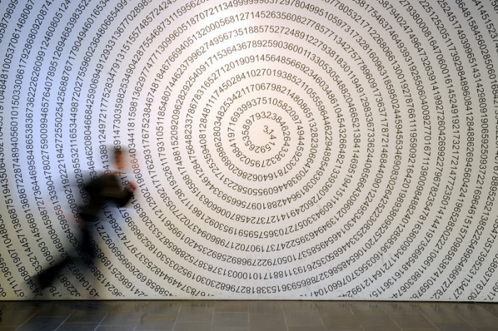 Ein Schulkind läuft im Mitmachmuseum «Mathematikum» an der auf eine Wand geschriebenen Kreiszahl Pi vorbei. Foto: Uwe Zucchi/dpa