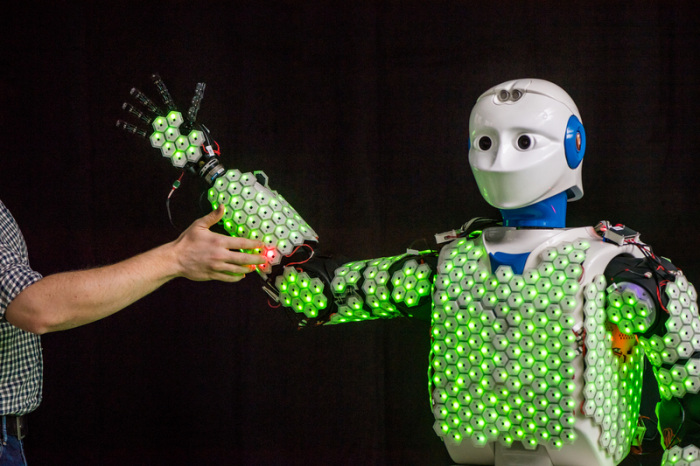 Der Arm eines Wissenschaftlers berührt einen humanoiden Roboter der Technischen Universität München mit künstlicher Haut. Foto: Astrid Eckert/Technische Universität München/dpa