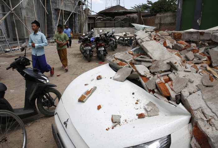 Bewohner gehen vorbei an eingestürzten Häusern. Foto: epa/Adi Weda