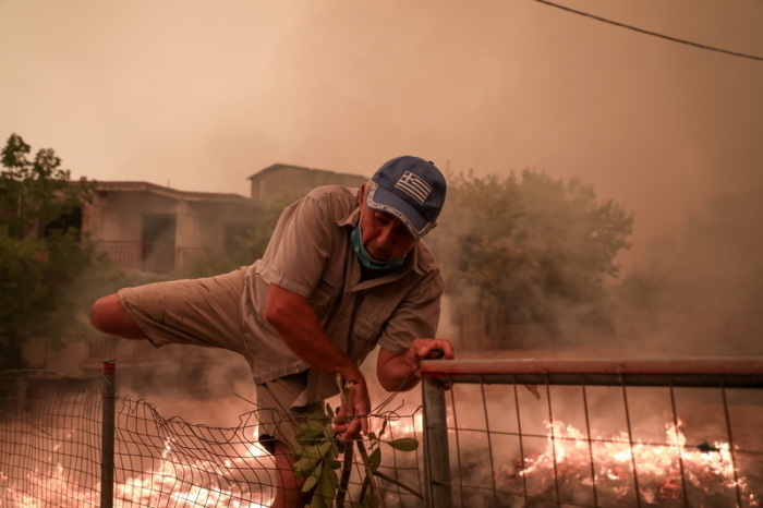 Ein Mann rettet sich während der Löscharbeiten eines Waldbrandes im Dorf Pefki auf der Insel Euböa über einen Zaun. Die Lage wird immer bedrohlicher: Auf der griechischen Insel Euböa stehen auch am siebten Tag gew... Foto: Eurokinissi/Eurokinissi