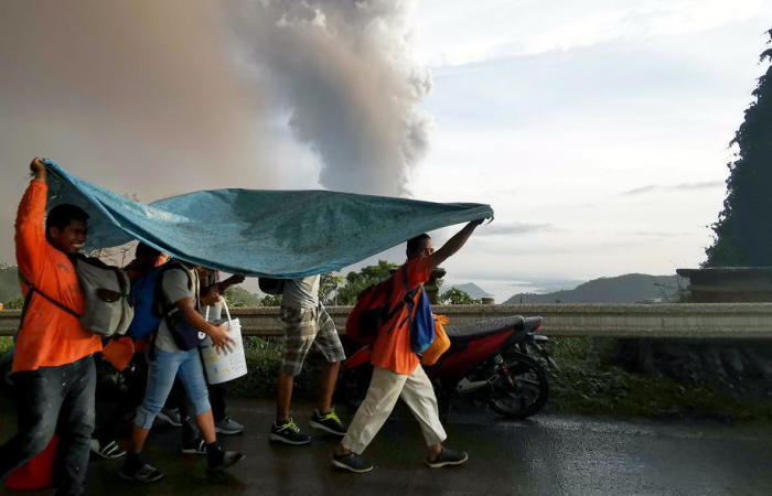 Menschen gehen unter einer großen Plastikplane in Deckung, als eine Aschesäule vom ausbrechenden Taal-Vulkan über Tagaytay City aufsteigt. Foto: epa/Francis R. Malasig