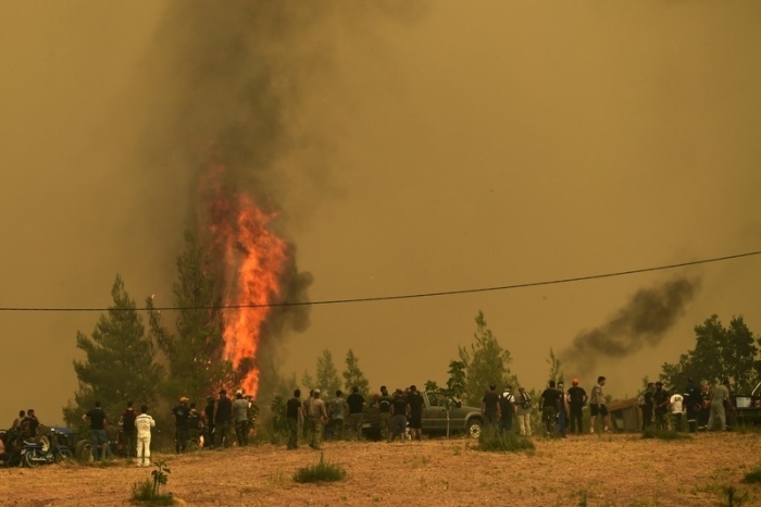Menschen beobachten die Flammen, die Bäume während eines Waldbrandes im Dorf Avgaria auf der Insel Euböa verbrennen. Foto: Michael Varaklas/dpa
