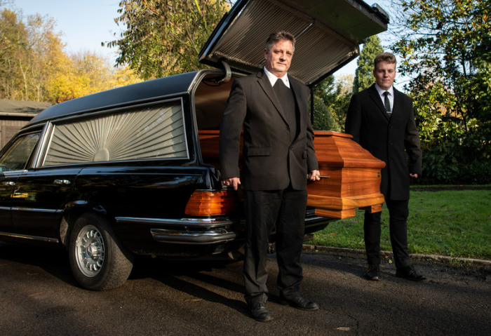 Bestatter Michael Wasch und sein Sohn und Sargträger Patrice heben einen Sarg aus einem Leichenwagen. Foto: Bernd Thissen/Dpa