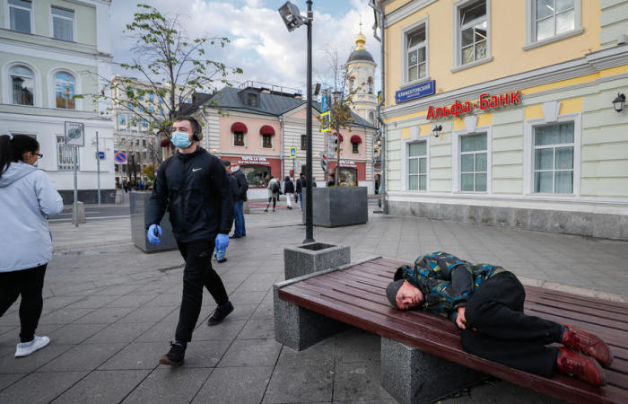In Moskau geht ein Mann mit einer schützenden Gesichtsmaske an einem Obdachlosen vorbei, der auf einer Bank schläft. Foto: epa/Juri Kotschetkow