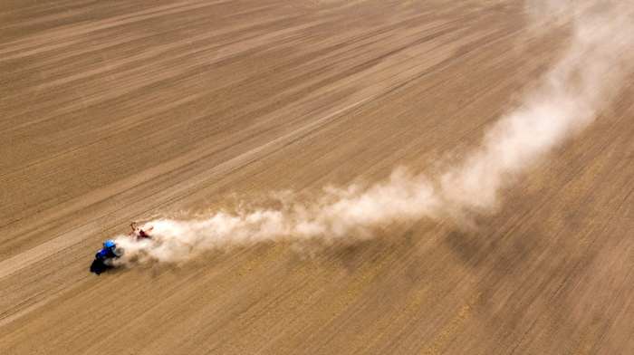 Ein Traktor fährt mit einer Sämaschine über ein Feld und zieht eine riesigen Staubwolke hinter sich her. Foto: Jan Woitas/Dpa-zentralbild/dpa