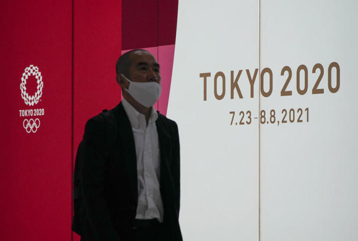 Ein Passant, der eine Schutzmaske trägt, geht an dem Emblem und dem Zeitplan der Olympischen Spiele von Tokio 2020 vorbei. Foto: epa/Kimimasa Mayama