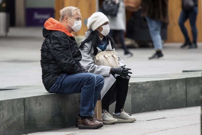 Zwei Schutzmasken tragende Personen sitzen auf dem Stephansplatz in Wien. Foto: epa/Christian Bruna
