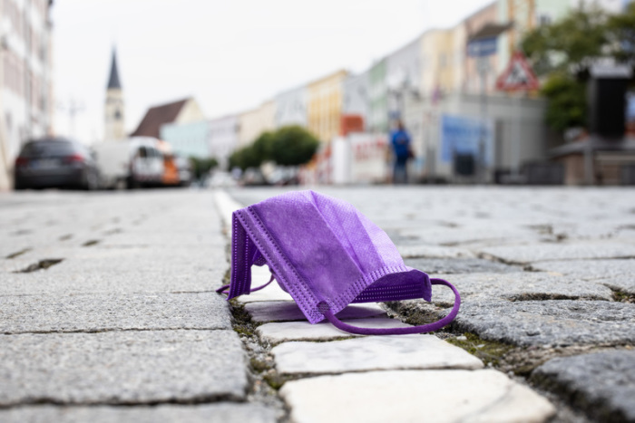 Eine violette medizinische Maske liegt auf einer Straße. Foto: Matthias Balk/dpa
