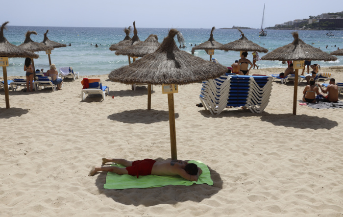 Ein Mann liegt unter einem Sonnenschirm am Strand von Cala Major. Foto: Clara Margais/dpa