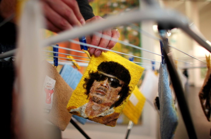 Ein Konservator hängt einen Waschlappen auf, auf dem das Porträt des ehemaligen libyschen Diktators Muammar al-Gaddafi gemalt ist. Foto: epa/Oliver Berg