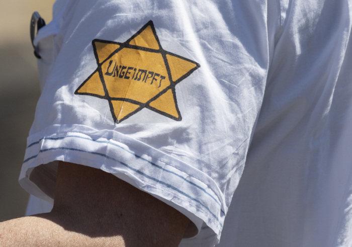 «Ungeimpft» steht auf einem nachgebildeten Judenstern am Arm eines Mannes, der versucht hatte, sich unter die Teilnehmer einer Demonstration zu mischen, die sich auch gegen Verschwörungstheorien zum Corona-Virus wendet. Foto: Boris Roessler/dpa