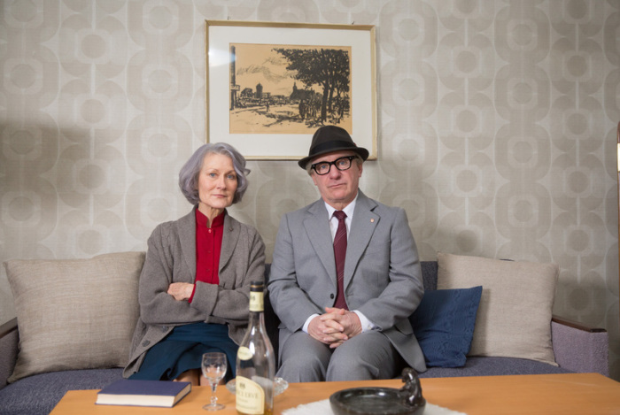 Die Schauspieler Hedi Kriegeskotte und Jörg Schüttauf in den Rollen von Margot und Erich Honecker sitzen in einem Wohnzimmer bei den Dreharbeiten zur Krimikomödie 
