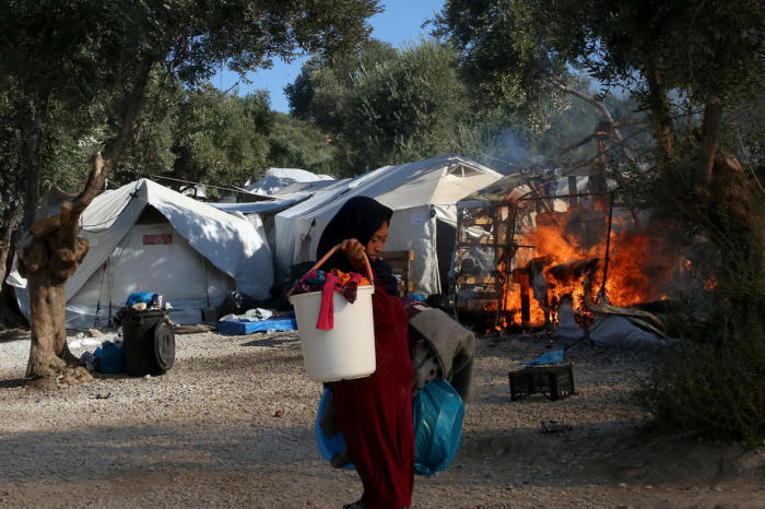 Ein Asylbewerber trägt Habseligkeiten vor einem Feuer im Flüchtlingslager Moria auf der Insel Lesbos weg. Foto: epa/Orestis Panagiotou