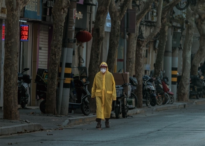 In Shanghai geht ein Mann, der zum Schutz eine Maske und einen Regenmantel trägt, auf einer menschenleeren Straße. Foto: epa/Alex Plavevski