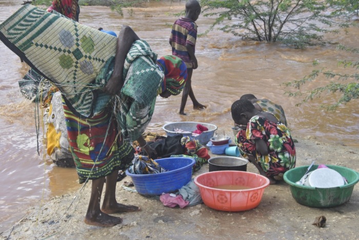 Eine vertriebene Frau und Kinder waschen ihre Haushaltsgegenstände mit Flutwasser. EPA-EFE/STR.