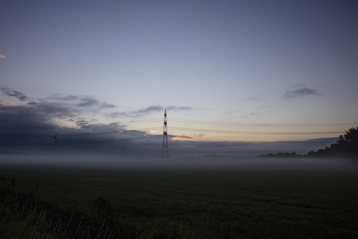 Ein Strommast ist auf einem Feld vom Morgennebel umgeben. Foto: Frank Molter/dpa