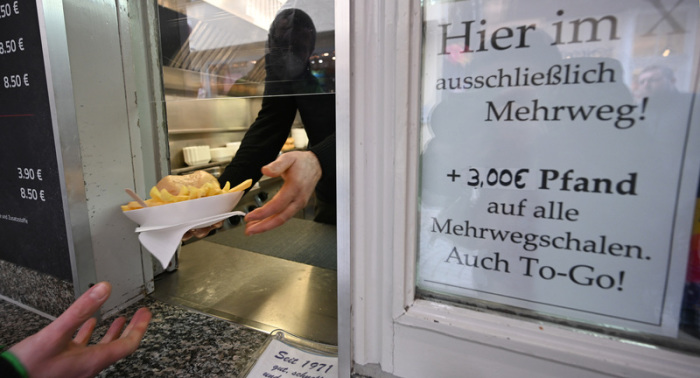Eine Hand hält an einem Imbiss in der Innenstadt einen Mehrwegteller mit Pommes und einem Burger. Kunden haben künftig ein Anrecht darauf, ihre To-Go-Speisen und -Getränke in einer Mehrwegverpackung zu bekommen. Foto: Bernd Weißbrod/dpa
