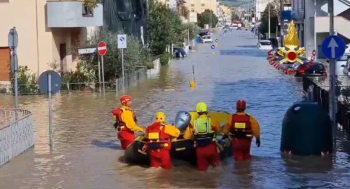 Feuerwehrleute schieben ein Schlauchboot durch eine überflutete Straße. Foto: Vigili del Fuoco/dpa