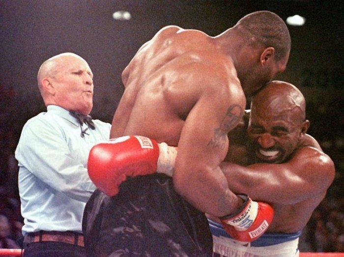 Der damalige Weltmeister im Schwergewicht, Evander Holyfield (r), verzieht das Gesicht, nachdem ihn sein Herausforderer Mike Tyson (M) ins Ohr gebissen hat. Foto: Jeff Haynes/epa