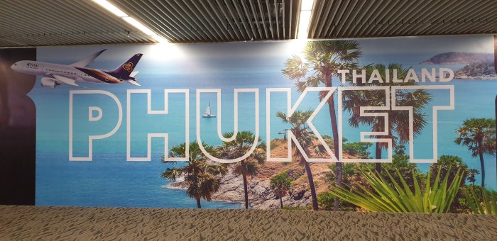 Ein Werbebanner am Flughafen Phuket begrüßt Reisende mit tropischen Motiven und einem Flugzeug der Thai Airways. Foto: Rüegsegger