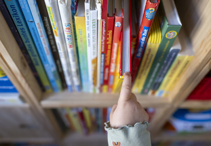 Ein Mädchen zieht in einem Kinderzimmer in Leipzig ein Kinderbuch aus einem Regal. Foto: Hendrik Schmidt/dpa