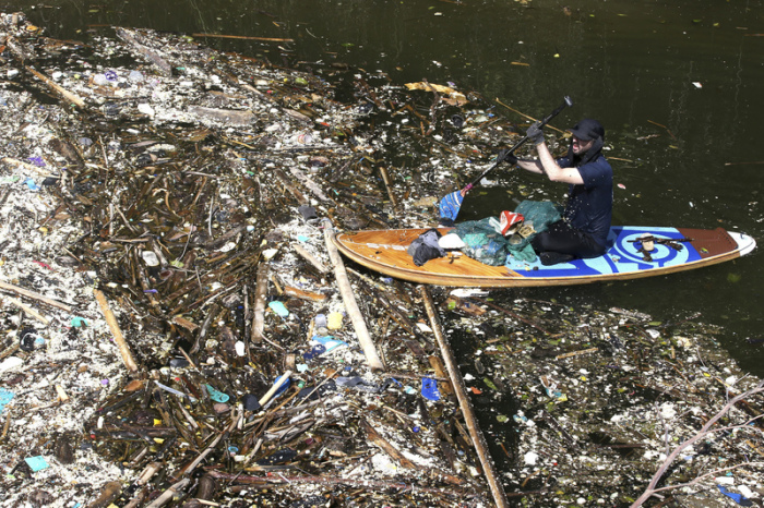 Ein Freiwilliger, der auf einem Paddelbrett sitzt, sammelt auf einem Fluss in Pecatu Müll auf. Während der Monsunzeit sind einige Flüsse mit Plastikmüll und Unrat übersät. Foto: Firdia Lisnawati/Ap/dpa