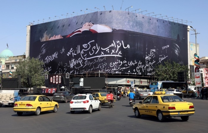Fahrzeuge passieren auf dem Enghelab-Platz in Teheran ein antiamerikanisches Plakat mit einer Darstellung von US-Präsident Donald Trump. Foto: Abedin Taherkenareh/epa