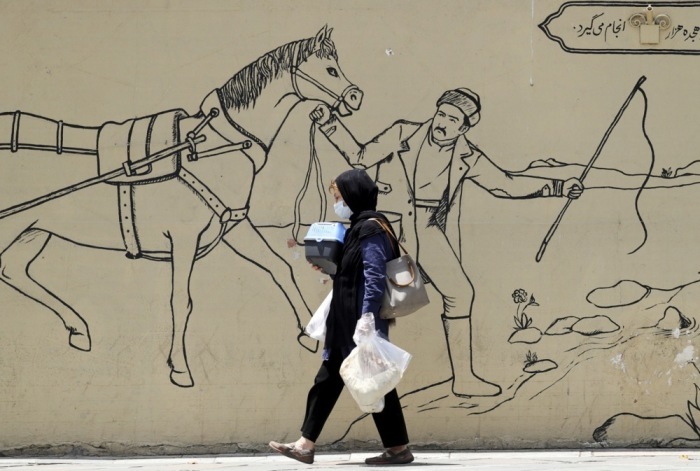 Eine Frau aus dem Iran trägt ihre Habseligkeiten, während sie neben einem Wandgemälde in einer Straße in Teheran geht. Foto: epa/Abedin Taherkenareh