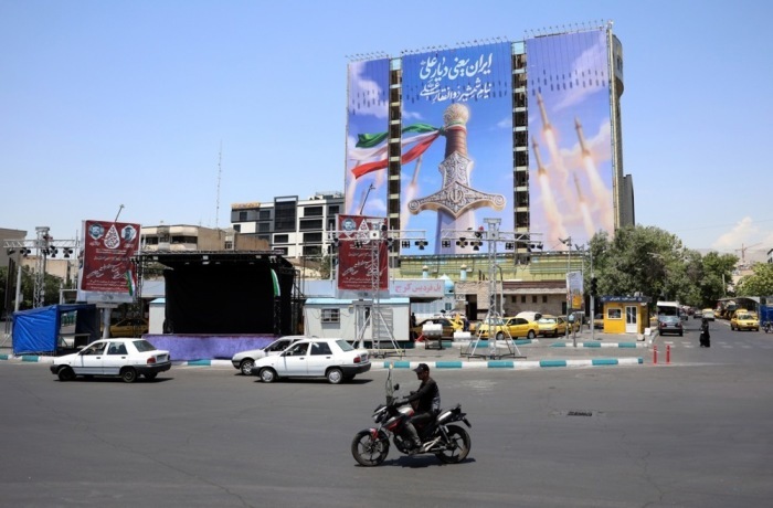 Autofahrer passieren auf dem Vanak-Platz in Teheran ein riesiges Propagandaplakat mit Raketenmotiven während der Spannungen zwischen Iran und den USA. Foto: Abedin Taherkenareh/epa/dpa