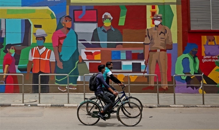 In Indien fahren Radfahrer mit Gesichtsschutzmasken an einem Wandgemälde in Bangalore vorbei. Foto: epa/Jagadeesh Nv
