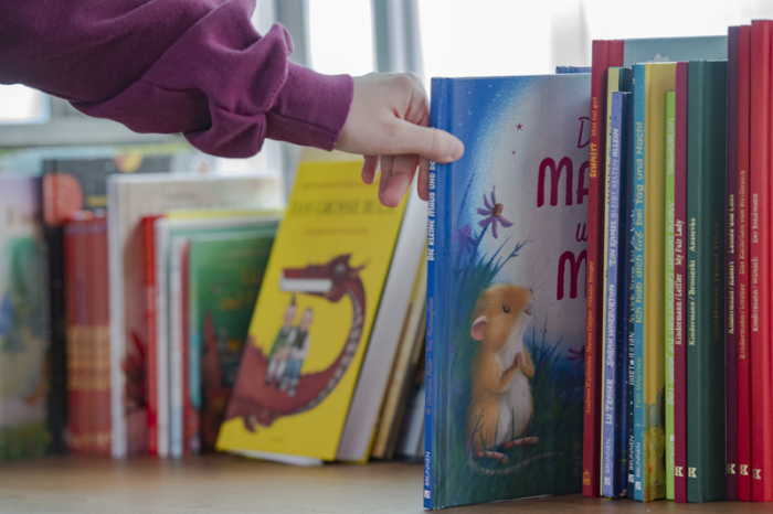 Eine Frau greift nach einem Kinderbuch. Foto: Paul Zinken/dpa
