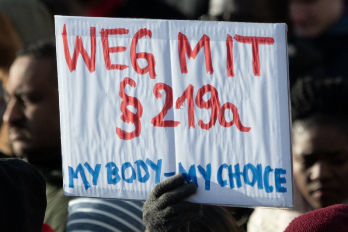 Teilnehmer einer Demonstration zum Internationalen Frauentag gehen durch Mitte und halten dabei ein Schild mit der Aufschrift «Weg mit Paragraf 219a - My Body - my Choice». Foto: Ralf Hirschberger/dpa