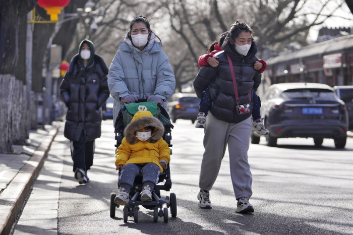 Frauen mit Mund-Nasen-Schutz gehen mit ihren Kindern auf einer Straße in Richtung Verbotene Stadt. Foto: Andy Wong/Ap/dpa
