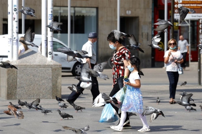 Ein Kind und eine Frau mit Gesichtsmasken spazieren zwischen Tauben in Zagreb. Foto: epa/Antonio Bat