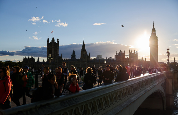 Zahlreiche Menschen stehen in der Abendsonne auf der im Augenblick für den Verkehr gesperrten Westminster Bridge über der Themse vor dem Parlament. Foto: Christian Charisius/dpa