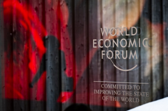Das Logo des WEF und die Reflexion einer KI-generierten Projektion sind abgebildet, während eine Frau am Schlusstag des 54. Jahrestreffens des Weltwirtschaftsforums (WEF) in Davos vorbeigeht. Foto: epa/Gian Ehrenzeller